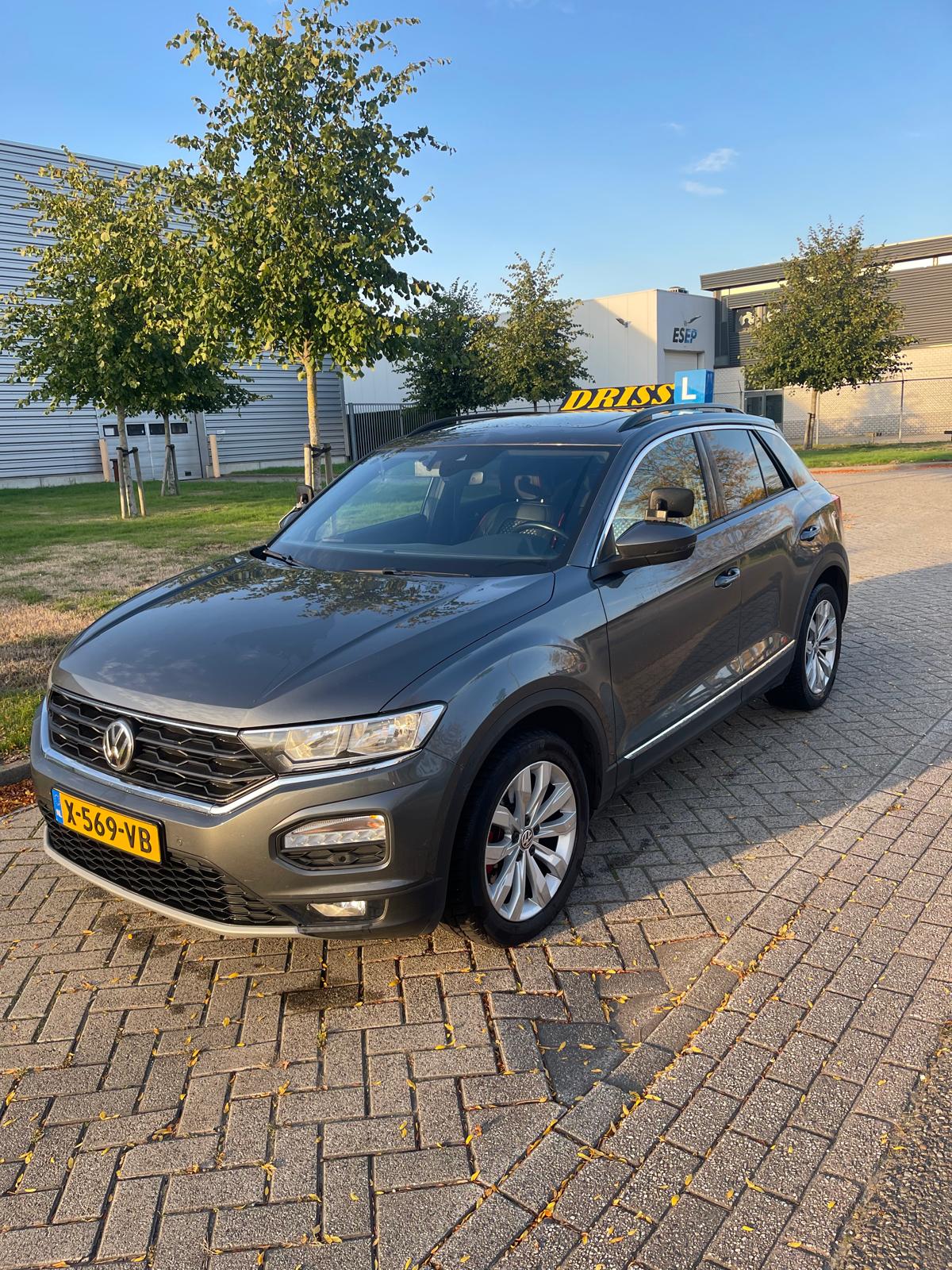 De lesauto van Rijschool Driss: een grijze Volkswagen T-Roc met het gele DRISS-dakbord